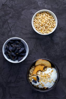 Sağlıklı ev yapımı kahvaltı yulaf ezmesi, doğal Yunan yoğurdu, fındık ve kuru üzümlü koyu gri arka planda.
