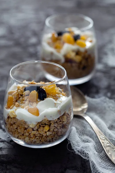 Homemade organic fresh greek yogurt parfait with granola,nuts and raisins in glass on gray concrete background