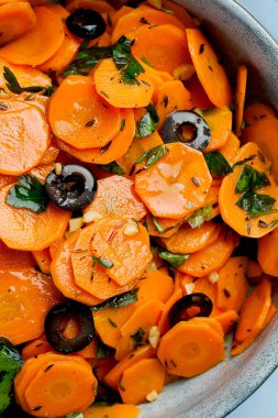 Geleneksel Fas usulü havuç salatası Kuzey Afrika vegan yemeği doğranmış maydanoz ve gri tabakta zeytin.