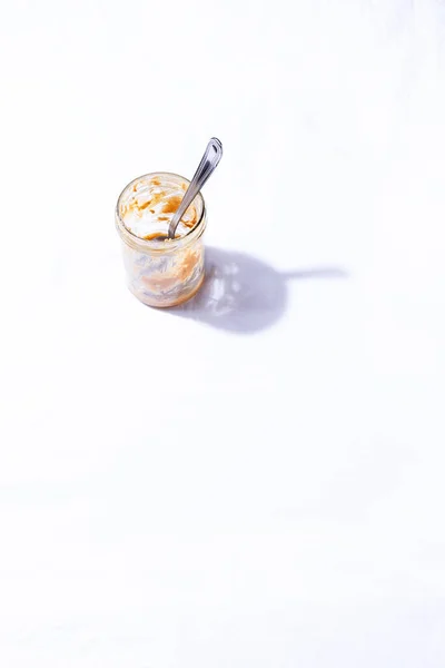 Frasco vazio de manteiga de amendoim com colher dentro no fundo da mesa branca — Fotografia de Stock