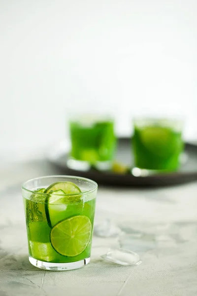 Homemade iced matcha green tea or lemonade with cucumber and lime on light gray background
