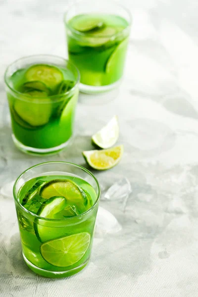 Homemade iced matcha green tea or lemonade with cucumber and lime on light gray background