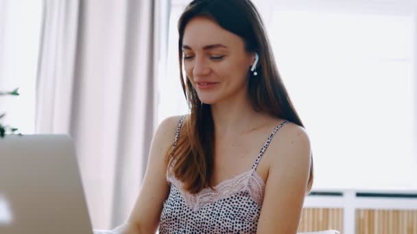 Happy sorrindo linda menina em roupa de noite sentar-se à mesa na manhã ensolarada digitando mensagem no laptop ouvir música enviando e-mail em fones de ouvido sem fio desfrutando croissant crocante para brunch café fresco — Vídeo de Stock