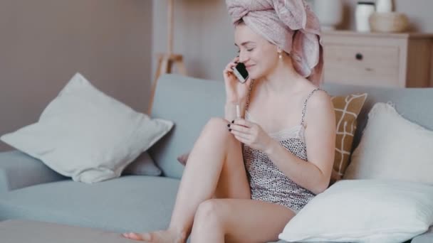 Belle fille assise sur le canapé dans l'appartement va faire la fête, peint des ongles avec du vernis pédicure — Video