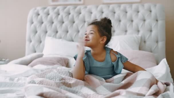Africano americano preto bela menina sorridente filha sentar-se em confortável cama de luz com colchão ortopédico no quarto brilhante bebê jovem de bom humor acenando olhando para a câmera em estado alegre brincalhão — Vídeo de Stock