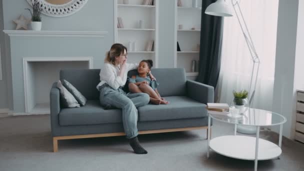 Happy young caring mother on couch talking smart pretty african american daughter with curly black hair in blue dress — Stock Video