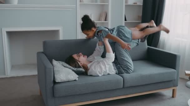 Przyjazny piękna rodzina zdrowa młoda matka podnoszenie fajne dziecko córka w górę grając samolot na kanapie w mieszkaniu, śmieszne dziecko dziewczyna zabawy razem latać w ramiona matki ćwiczyć acro para joga bonding — Wideo stockowe
