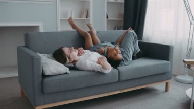 Kanepede genç, sıska, harmonik bir kadın, modern daire konseptinde çocuk sorunlarını tartışır. Aile dostu, neşeli kız, annesinin karnına uzanmış, aktif çocuk annesiyle eğleniyor.