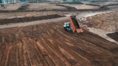 Grund, yüksek katlı apartman manzarasına hazırlanmak için kum kamyonu traktöründeki drone 'dan kuma çakıl döker ve bir apartman dairesi inşaatı için kumsal taşı döker.