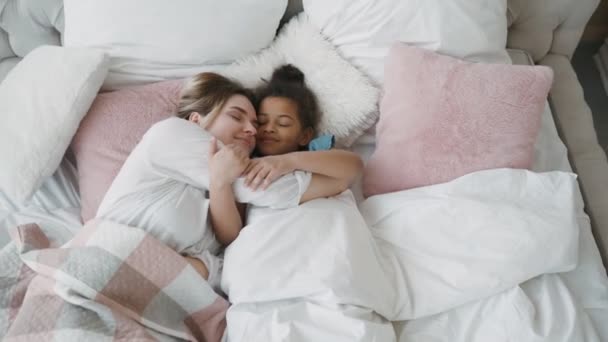 照片上的木乃伊和黑人女孩躺在舒适的公寓里，白天睡在床上，俯瞰着迷人的年轻妈妈，与快乐的非洲裔美国女儿躺在床上笑着 — 图库视频影像