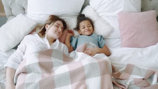 Семья спешит просыпаться быстро, чтобы выполнить свои планы на день или идею приходят в голову сверху вниз вид кровати, заботясь молодая мама мама мама улыбается лежа в постели с радостным афроамериканской дочери — стоковое видео