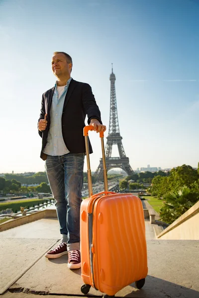 Handsome man woman with orange suitcase standing on Trocadero square. Paris cityscape, view of Eiffel Tower. Travel concept