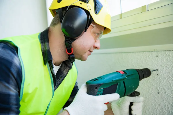 Male construction worker in hard hat drilling concrete wall with a drill. Building and renovation.