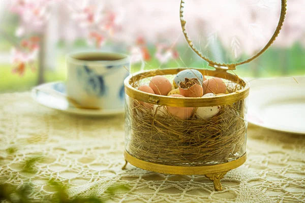 Beautiful served small table with Easter decorations on outdoor terrace. Little chocolate bunny with bow, chocolate eggs, cup of coffee, crystal bowl. Spring holiday setting. Close-up