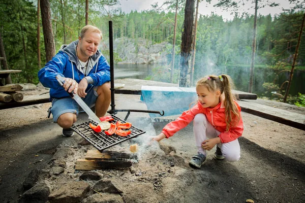 湖の岩場の海岸の森でバーベキューをしている男と彼の小さな娘は 焼きパン マシュマロを作っています フィンランドを探検する家族 北欧の夏の風景 — ストック写真