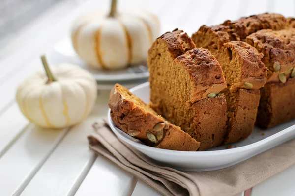 Pumpkin bread, cake on a white plate, on a kitchen beige napkin, on a white wooden background, with cooking utensils, with forks, side view, with pumpkins, close-up.