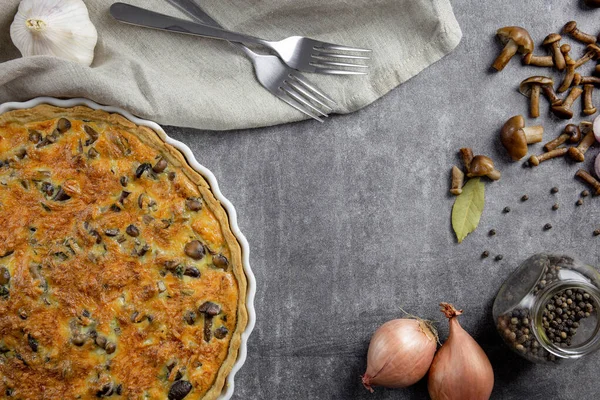 Traditional french pie Quiche Lorraine with mushrooms, potatoes, cheese, onions and seasonings. In a white baking dish, with forks, with black pepper and bay leaf, on a concrete background.Top view. — 스톡 사진
