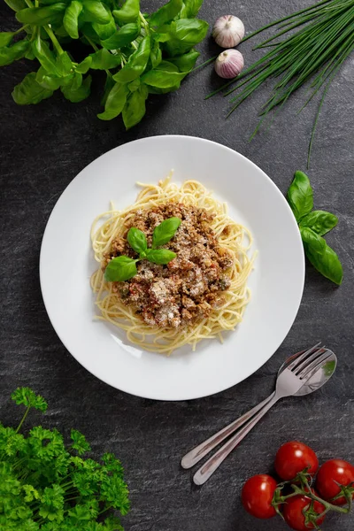 Παραδοσιακό ιταλικό σπαγγέτι Μπολονέζ με κρέας και σάλτσα ντομάτας σε πιάτο. Τυρί παρμεζάνας, φρέσκες ντομάτες, βασιλικό, μπαχαρικά και βότανα. Σκοτεινό φόντο. Άνω όψη. — Φωτογραφία Αρχείου