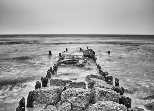 Zwart-wit foto van een oude golfbreker op een strand. — Stockfoto