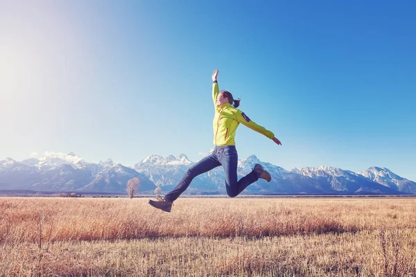 Szczęśliwa młoda kobieta, skoki na łąki górskie o zachodzie słońca. — Zdjęcie stockowe