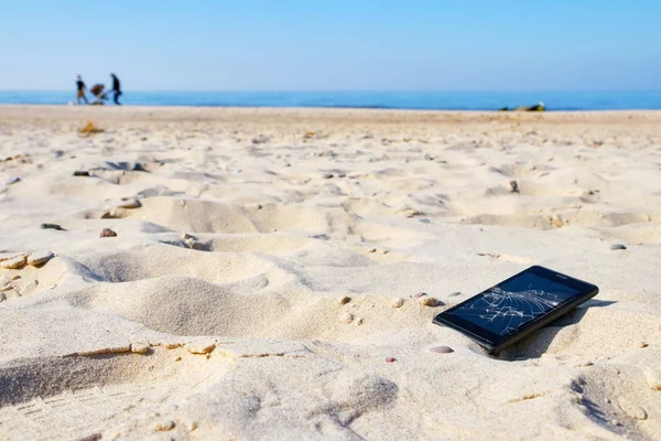 Teléfono móvil con pantalla rota en arena en una playa . — Foto de Stock