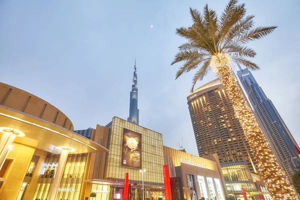 Opzoeken van uitzicht op de verlichte palmbomen, Dubai Mall en Burj Khalifa gevel in de schemering. — Stockfoto