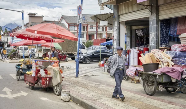 Pedestrian passes a food vendor with bicycle stall on a street of Lijiang. — Stock Photo, Image