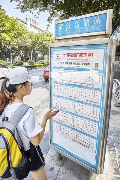 Chinese woman with backpack checks the timetable at the bus stop. — Stock Photo, Image
