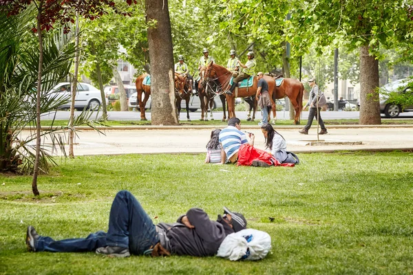 La gente descansa en un parque municipal con policía montada a distancia . — Foto de Stock