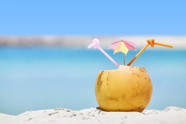 Кокосовый коктейль с красочным зонтиком и соломинками на пляже — стоковое фото