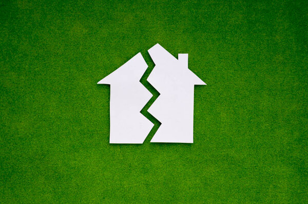 The white paper house is split in half against the green grass. The concept of business, Finance, property division.