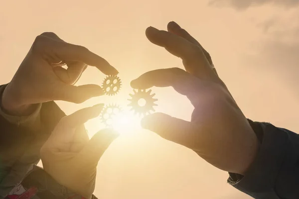 Three gears in the hands of people against the sky. Ideas, interaction, teamwork.