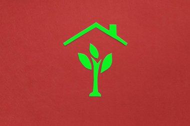 Bir evin çatısının altında filizlenen bir ağaç kırmızı arka planda yeşildir. Çevresel olarak güvenli konut.