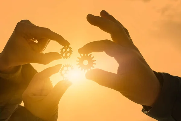 Three gears in the hands of a group of people against the background of the evening sky. interaction, teamwork.