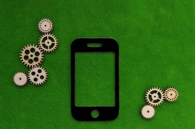 Siyah renkli cep telefonu, yeşil arka planda ahşap dişliler. Etkileşim, mekanizma, mobil iletişim.