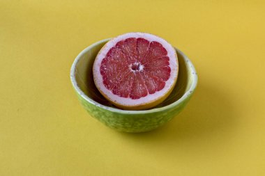 Bir kasede yarım greyfurt; sarı arka plan.