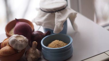 Camın arkasında kil sürahiler, mısır gevreği, soğan ve sarımsak var.