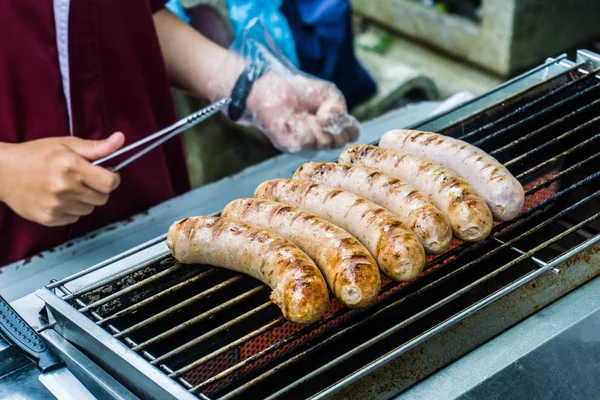 Salsicha fresca e cachorros-quentes grelhando ao ar livre em um churrasco a gás — Fotografia de Stock