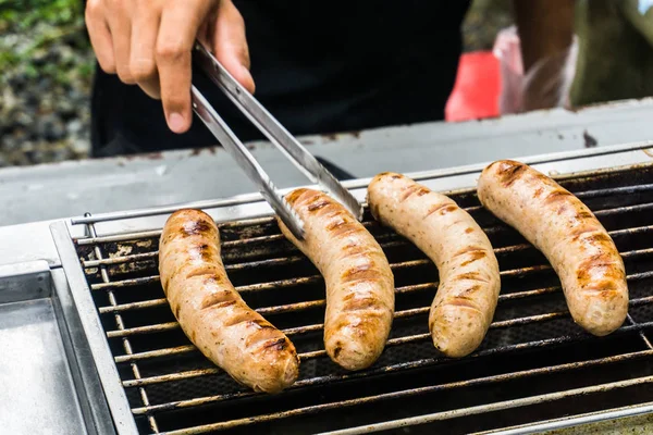 Salsicha fresca e cachorros-quentes grelhando ao ar livre em um churrasco a gás — Fotografia de Stock