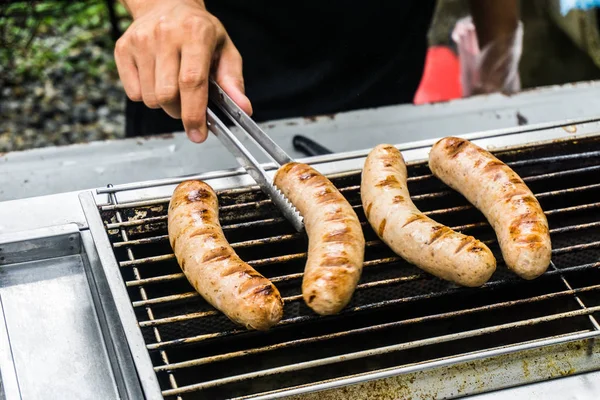 Salsicha fresca e cachorros-quentes grelhando ao ar livre em um churrasco a gás — Fotografia de Stock