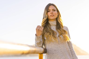 Deniz kıyısında genç ve güzel bir kadının günbatımı portresi.