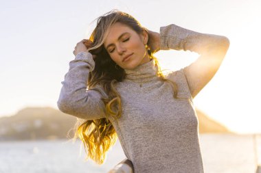 Deniz kıyısında genç ve güzel bir kadının günbatımı portresi.