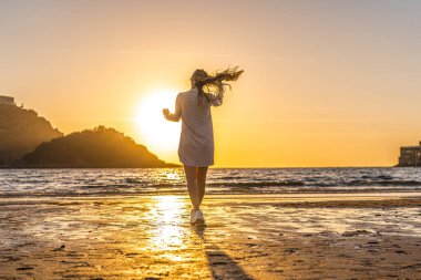 Deniz kıyısında genç ve güzel bir kadının günbatımı portresi.