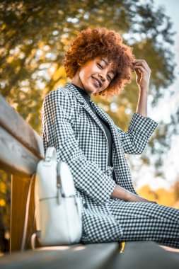 Parkta bankta oturan şık, genç ve çekici Afrikalı Amerikalı kadın.