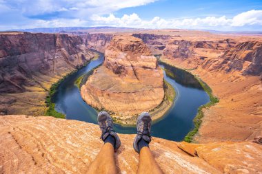 Turist dinleniyor ve arka planda Horseshoe Bend ve Colorado Nehri 'ne bakıyor.