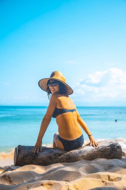 Bikinili güzel bir kız ve hasır şapkalı deniz kenarında bir kütükte oturuyor Tela, Honduras 'ta Punta Sal plajında.