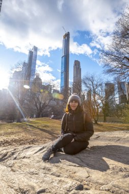 Genç gülümseyen turist kışın Central Park 'ta oturuyor.