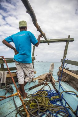 Wasini, Kenya - Ağustos 2018: Geleneksel Wasini teknesinin önünde denize bakan mavi tişörtlü Afrikalı adam