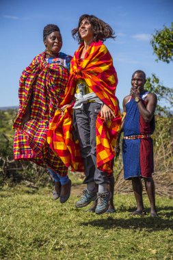 Masai Mara, Kenya - August 2018: Local and Caucasian tourists with young Masais