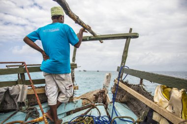 Wasini, Kenya - Ağustos 2018: Geleneksel Wasini teknesinin önünde denize bakan mavi tişörtlü Afrikalı adam